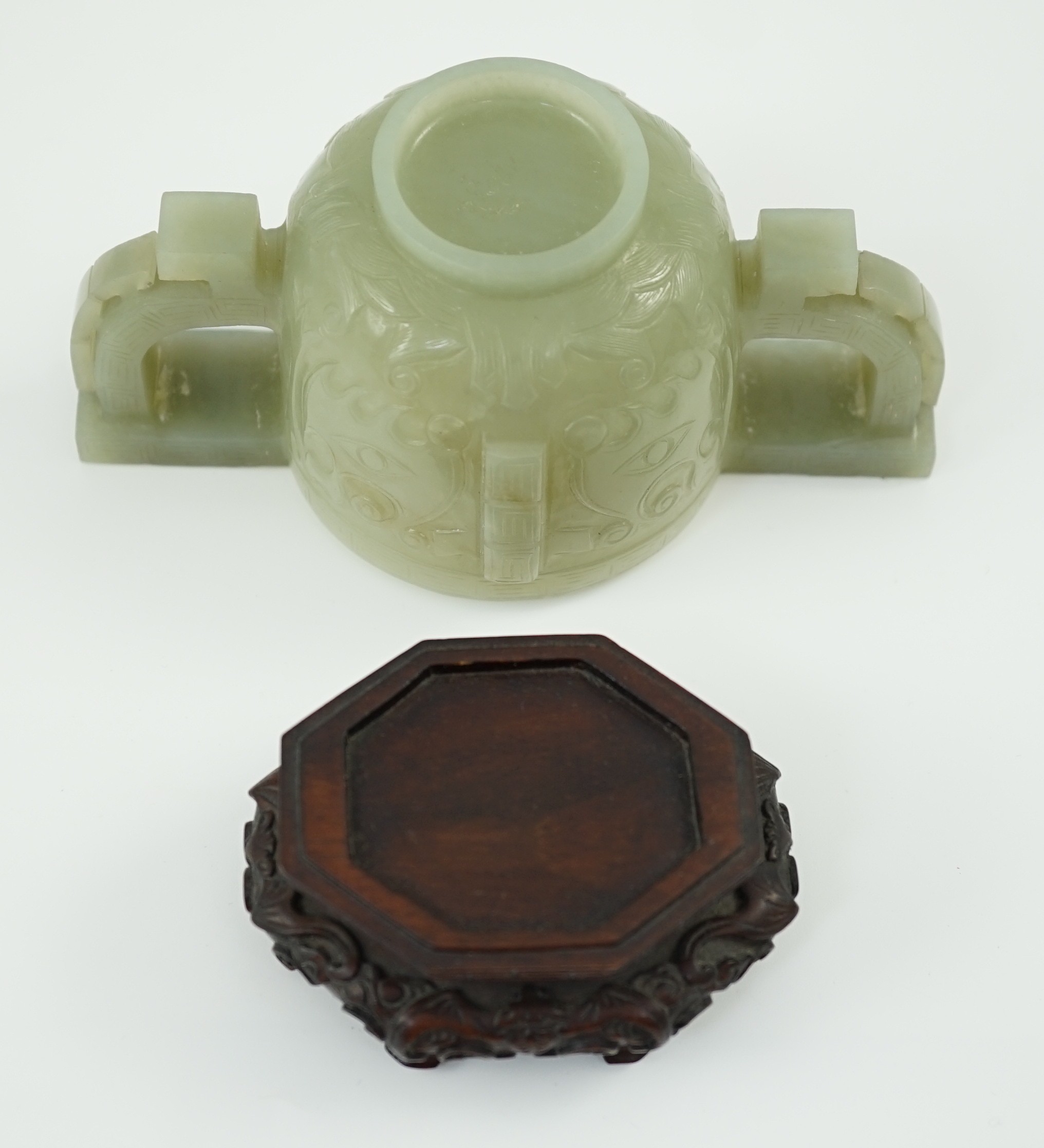 A Chinese archaistic celadon jade two handled cup, 17th century, 12.9cm across 6.1cm high, associated wood stand